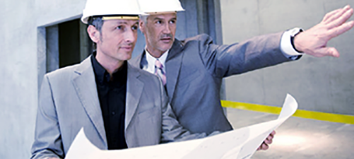 Two men surveying a construction site with blueprints
